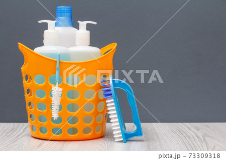 Bottles of dishwashing liquid in a basket with brush on wooden desk. 73309318