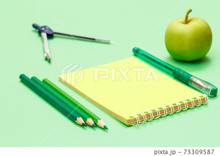 Compass, color pencils, notebook, pen and apple on the green background. Compass, color pencils, notebook, pen and apple on the green background. 73309587