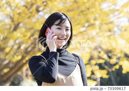 秋の公園で笑顔で電話する女性 73309617