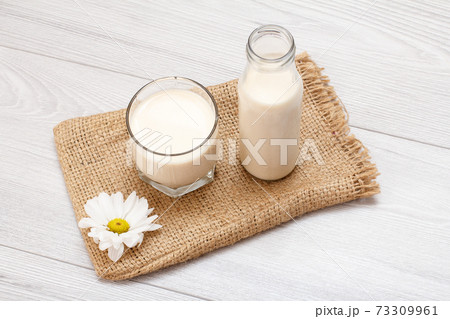 Bottle and glass of milk, chamomile flower on gray background. Bottle and glass of milk, chamomile flower on gray background. 73309961