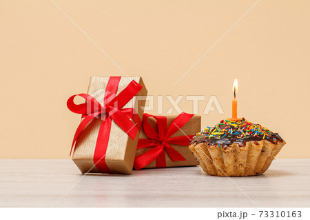 Tasty birthday muffin with burning festive candle and gift boxes. Tasty birthday muffin with burning festive candle and gift boxes. 73310163