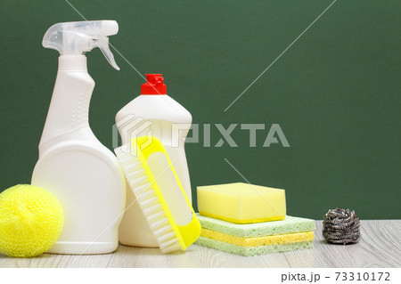 Bottles of dishwashing liquid, brush and sponges on green background. 73310172