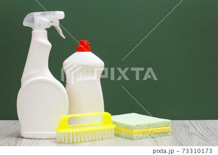 Bottles of dishwashing liquid, brush and sponges on the green background. 73310173