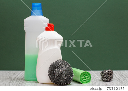 Bottles of dishwashing liquid, garbage bags and sponges on the green background. 73310175