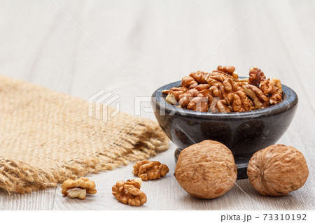 Walnuts in stone bowl with sackcloth on a wooden background. Walnuts in stone bowl with sackcloth on a wooden background. 73310192