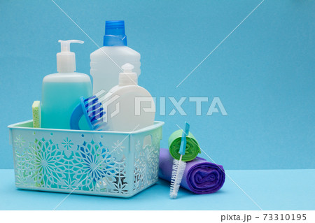 Bottles of dishwashing liquid in basket, sponges and brushes on blue background. Bottles of dishwashing liquid in basket, sponges and brushes on blue background. 73310195