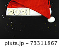 Wooden numbers 2021 on a red Santa hat on a black background. 73311867