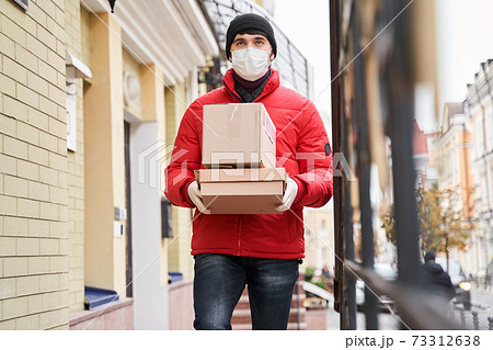 Courier wearing protective mask holding box near customer house Courier wearing protective mask holding box near customer house 73312638