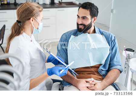 Dentist showing the paper to a smiling man client 73313566