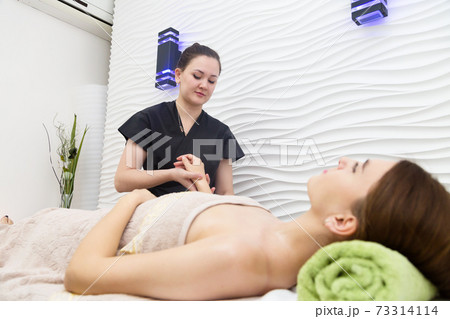 Masseur in black robe doing hand massage to a lying client Masseur in black robe doing hand massage to a lying client 73314114