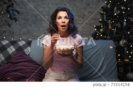 Young beautiful woman stay home, during pandemic, spends his free time watching TV on couch at home, wonder and scared. Girl watching projector movies with popcorn in evening 73314258