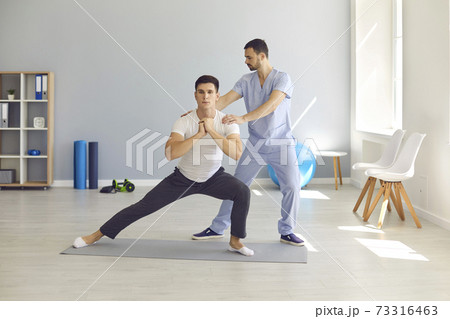 Physiotherapist helping patient do side lunges to develop balance, stability and strength 73316463