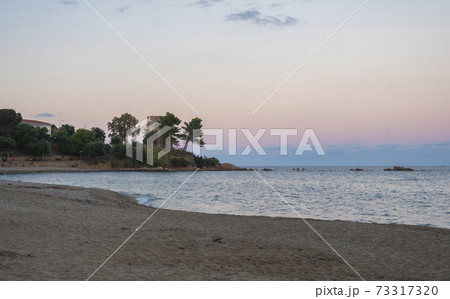 view of empty Spiaggia di Santa Maria Navarrese sand beach with green trees and old stone tower Torre Saracena in village Santa Maria Navarrese, Sardinia, Italy. Golden hour light view of empty Spiaggia di Santa Maria Navarrese sand beach with green trees and old stone tower Torre Saracena in village Santa Maria Navarrese, Sardinia, Italy. Golden hour light 73317320