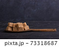 Cubes of cane sugar in a wooden spoon on a dark background 73318687