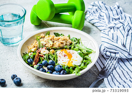 Quinoa salad with berries, poached egg and nuts, dumbbells on the background. Healthy post-workout food. 73319093