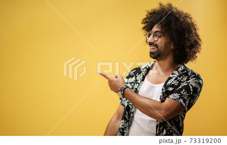 Portrait of mature man in a studio on yellow background, pointing fingers to copy space. 73319200