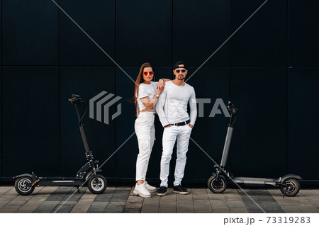 A girl and a guy are walking on electric scooters around the city, a couple in love on scooters. A girl and a guy are walking on electric scooters around the city, a couple in love on scooters. 73319283