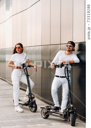 A girl and a guy are walking on electric scooters around the city, a couple in love on scooters. 73319286