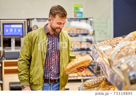 man chooses a fresh bread loaf in the supermarket 73319895