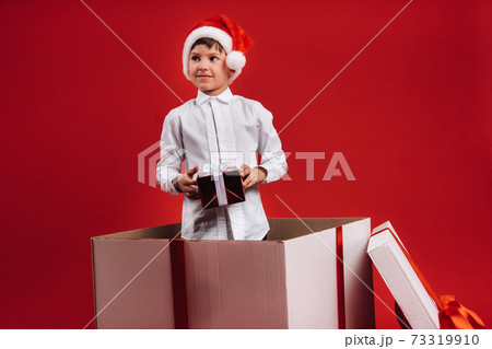 A little boy stands in a gift box with a Christmas present in his hands A little boy stands in a gift box with a Christmas present in his hands 73319910