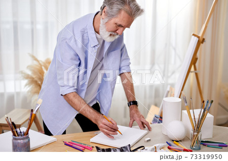 handsome skilled painter drawing sketch on sheet with pencil 73319950