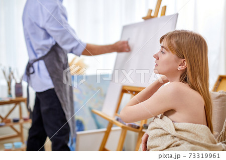 painter at the easel draws female model sitting on sofa 73319961