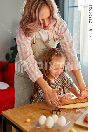 mother showing preschool daughter how to roll out dough for pie or cookies 73320001