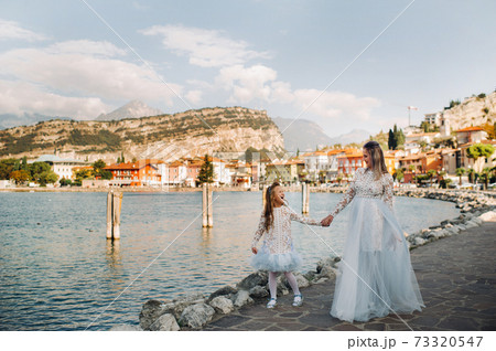 Italy, Lake Garda.Stylish Mother and daughter on the shores of lake Garda in Italy at the foot of the Alps. mother and daughter in Italy Italy, Lake Garda.Stylish Mother and daughter on the shores of lake Garda in Italy at the foot of the Alps. mother and daughter in Italy 73320547