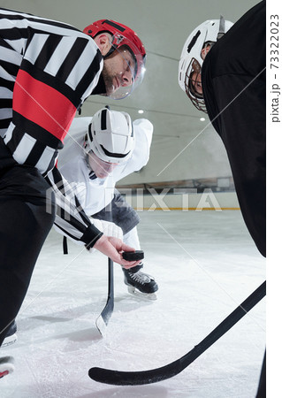 Hockey referee with puck looking at one of two players bending forwards 73322023