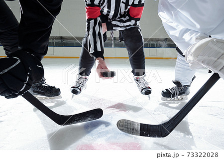 Hockey referee with puck standing on rink with two rivals on his right and left 73322028