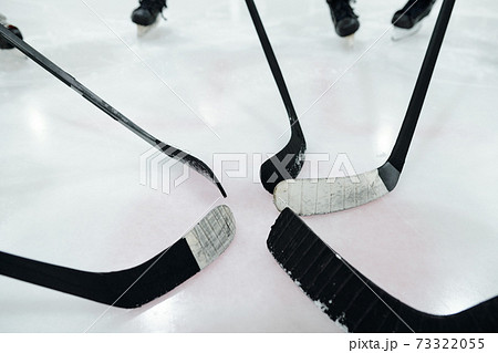 Hockey sticks in the middle of circle made up of players standing on ice rink Hockey sticks in the middle of circle made up of players standing on ice rink 73322055