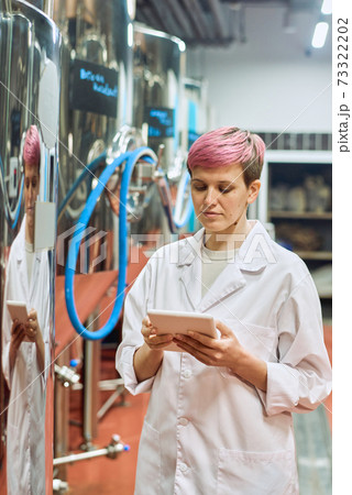 Young female brewery expert in whitecoat looking through data in tablet Young female brewery expert in whitecoat looking through data in tablet 73322202