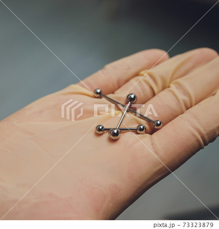 ear jewelry, piercing in hand with a disposable glove. ear jewelry, piercing in hand with a disposable glove. 73323879