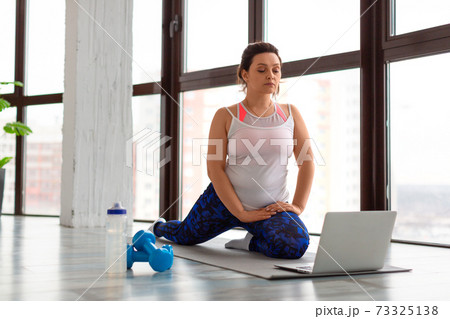 Home online workout concept. Middle aged woman stretching legs at home in front of laptop monitor. Home online workout concept. Middle aged woman stretching legs at home in front of laptop monitor. 73325138