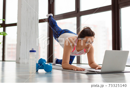 Home online workout concept. Middle aged woman working out at home in front of laptop monitor. Home online workout concept. Middle aged woman working out at home in front of laptop monitor. 73325140