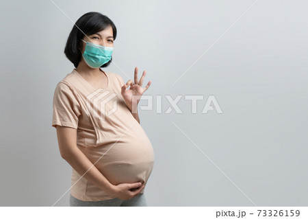 Smiling Asian Pregnant woman wearing protective face mask showing gesture OK sign Smiling Asian Pregnant woman wearing protective face mask showing gesture OK sign 73326159
