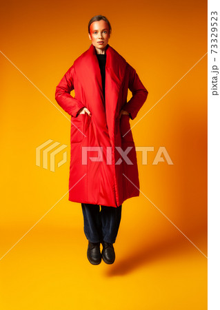 Trendy female in oversize coat jumping against yellow background Trendy female in oversize coat jumping against yellow background 73329523