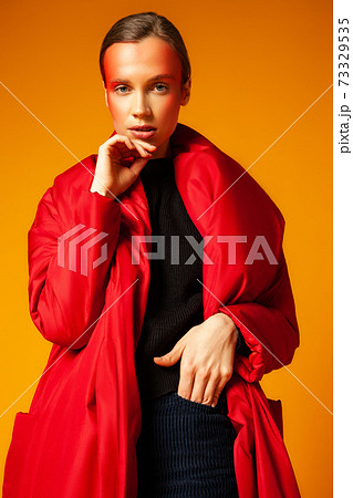 Woman in trendy coat touching face against yellow background Woman in trendy coat touching face against yellow background 73329535