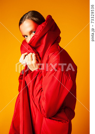 Young woman wrapping in red coat against yellow background Young woman wrapping in red coat against yellow background 73329536