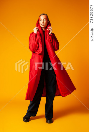 Female model adjusting trendy red coat against yellow background Female model adjusting trendy red coat against yellow background 73329677