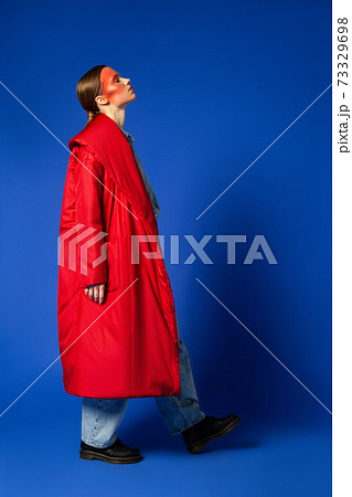 Female model in baggy coat walking against blue background Female model in baggy coat walking against blue background 73329698