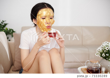 Woman with sheet mask on drinking tea 73330289