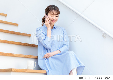 自宅の階段に座ってスマホを見る女性の写真素材