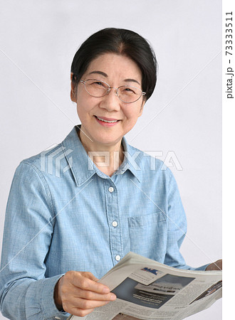 英字新聞を持つメガネをかけた笑顔のシニア女性　上半身 73333511