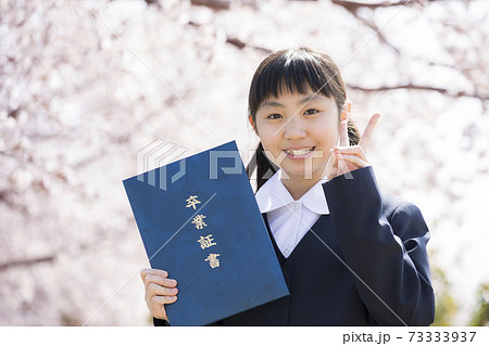 桜の前で卒業証書を持つ制服姿の女子小学6年生 卒業イメージの写真素材