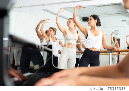 Multiethnic dancers training with one hand on barre under live music 73335353