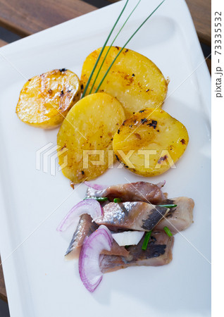 Fried potatoes with slices of mild-cured herring and onions served on plate Fried potatoes with slices of mild-cured herring and onions served on plate 73335532