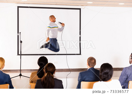 Expressive hispanic business coach speaking to audience and jumping 73336577