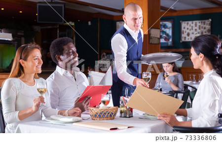 Smiling waiter serving aperitif to friendly company in restaurant 73336806