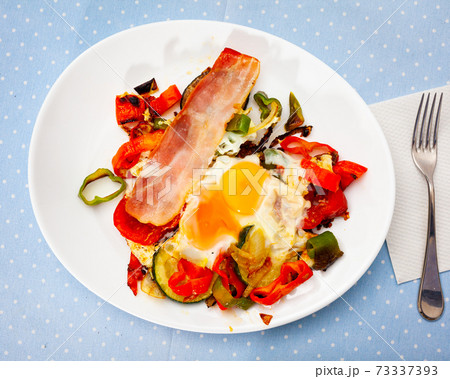 Scrambled eggs with bacon and vegetables served on plate 73337393